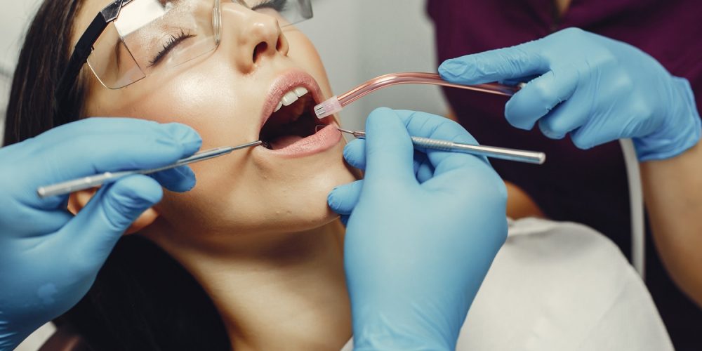 The dentist treats the girl's teeth. A young woman visited a dentist. The doctor works with an assistant